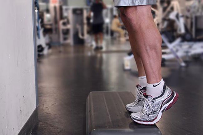 Stand facing the back of a sturdy chair, other support such as the back of a couch, or a wall bar at the gym.