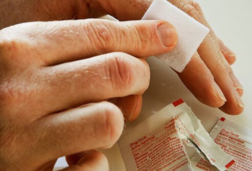 A man using antiseptic wipes to clean a wound on his finger.
