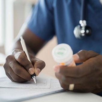A close-up of a doctor holding a bottle of pills and writing a prescription.