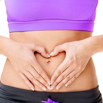 A woman makes a heart with her hands over her stomach.
