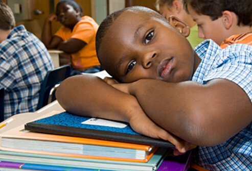 A boy daydreams in class while other students work.