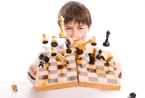 A boy intentionally ruins a game of chess by knocking pieces over.