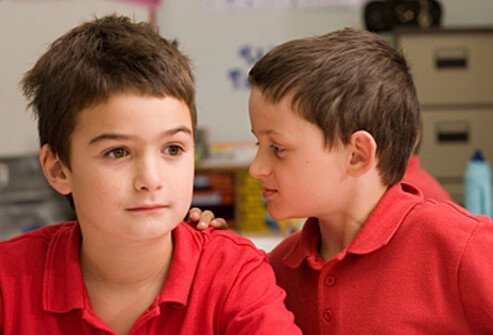 A boy interrupts another boy in a classroom.