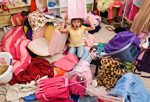 A girl sits in her disorganized and messy bedroom.