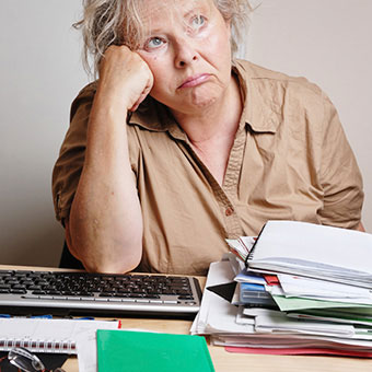 A frustrated woman sitting at a cluttered desk.