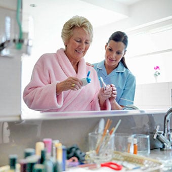 An nurse assists a senior woman brush her teeth.
