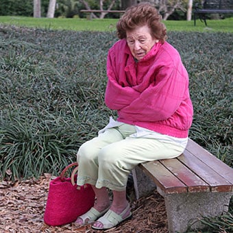 An elderly woman lost and shivering on a park bench.