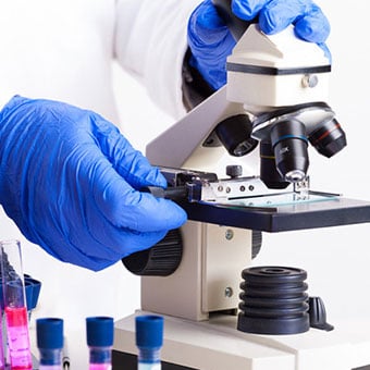 Lab technician viewing glass slide of blood sample.