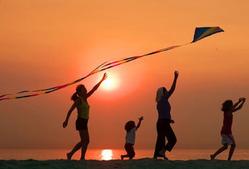 Photo of a woman getting active outdoors flying kite with kids.