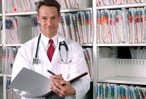 Doctor holding notebook standing next to files.