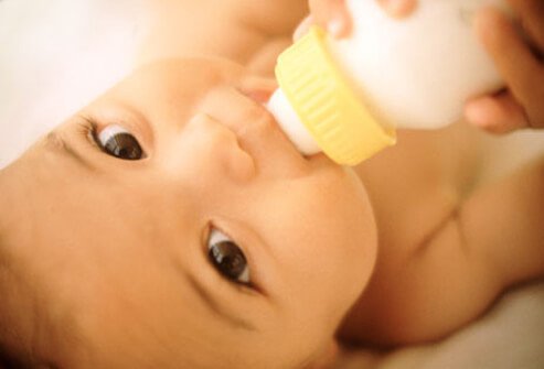 A baby holding drinking out of a baby bottle.