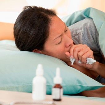 A woman with bronchitis coughs in bed.