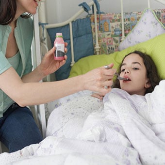 A mother gives her daughter cough medicine in bed.