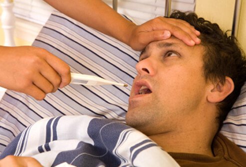 A man lying in bed with bronchitis about to have his temperature taken.