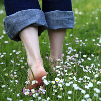 A woman walks barefoot through the grass.