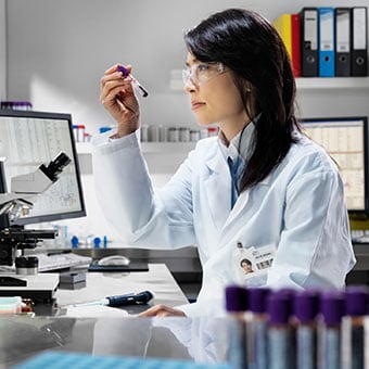 A laboratory technician examines a vial of blood.