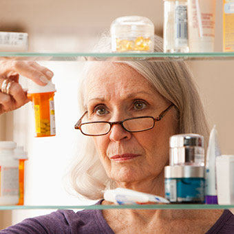 A woman looks at prescription medications in her medicine cabinet.