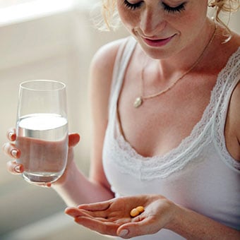 A woman holds medication and a glass of water.