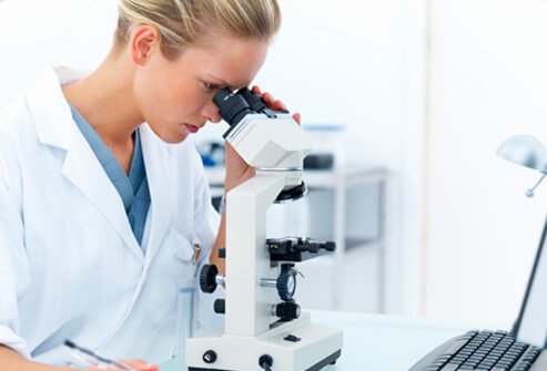 A female researcher looking into a microscope and writing notes.