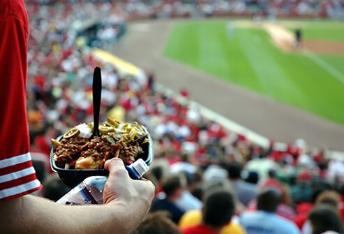 A man carries a tray of food down to his seat at the baseball park.