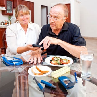 A healthcare professional discussing diet and showing a diabetic patient new technology for monitoring blood glucose levels on a smartphone or handheld device.