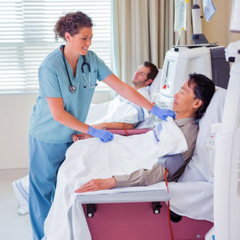 A female nurse looking after two patients undergoing renal dialysis.