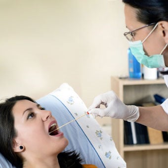 A doctor performs a throat swab on a woman with possible laryngitis.