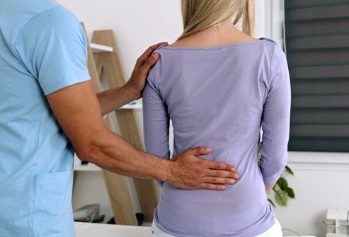 Picture of a healthprofessional with his hand on a patien'ts lower back.