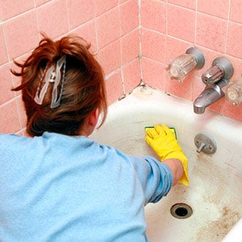 A woman cleans a moldy bathtub.