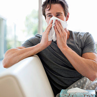 A man with allergies blows his nose into a tissue.
