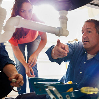 A plumber points out the mold to a homeowner as he works on pipes under the sink.