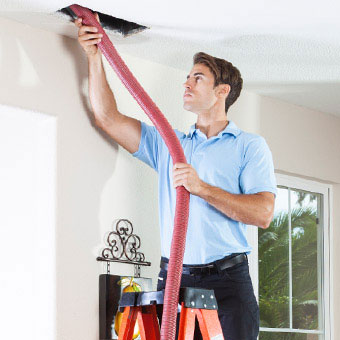 A man on a ladder removes mold from the ceiling vents.