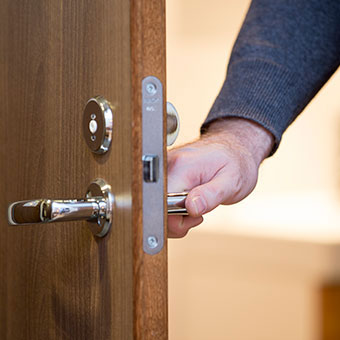 A man opens a door using the door handle. MRSA transmission can occur with objects such as door handles, floors, sinks, or towels that have been touched by a MRSA-infected person or carrier.