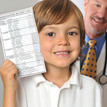 A young boy holds up his immunization record in the doctor's office.
