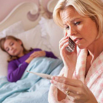 A mother reads a thermometer while her daughter is sick in bed.