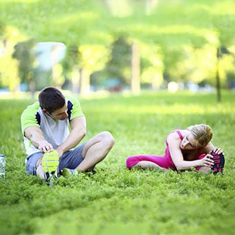 A male and female stretch in the park before their workout.