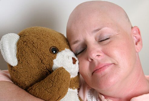Woman that has lost her hair from chemo treatment hugs a teddy bear.