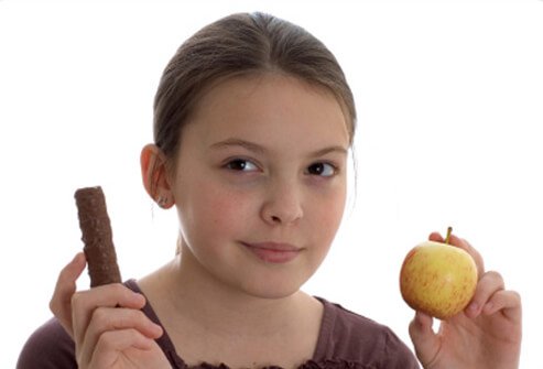 A young girl is tries to decide whether to eat a chocolate bar or an apple.