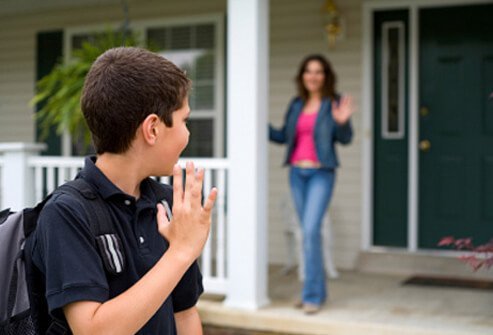 A son waves good-bye to his mother as he leaves for school.