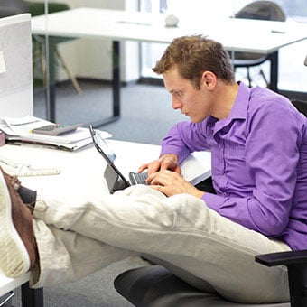 A male worker with poor sitting posture works on his computer at his desk.