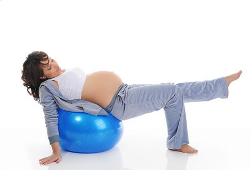 A pregnant woman performing an ankle rotation exercise on an exercise ball.