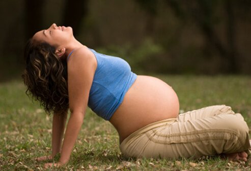 A pregnant woman stretching her back while sitting.