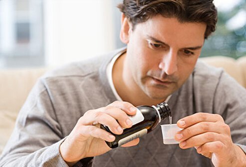 A man pours prescription cough syrup in to a cup.