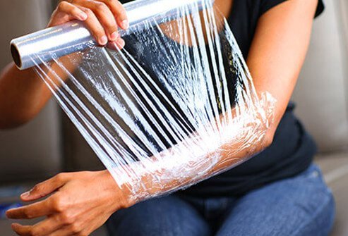 Woman wrapping her arm in plastic wrap.