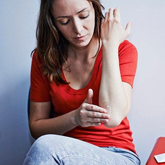 A woman rubs cream on an elbow rash.