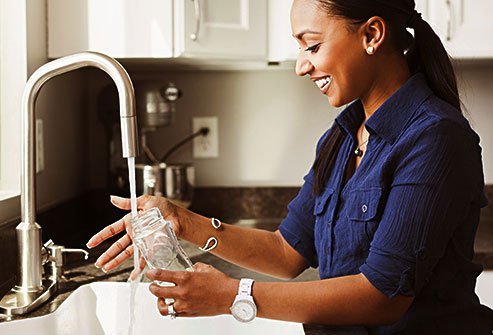 Woman washing bottle at kitchen sink.