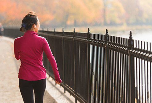 A woman walking outside along a park fence.