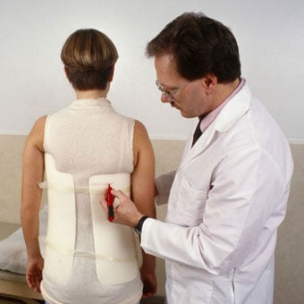 A scoliosis patient is fitted with a correcting brace by a doctor.