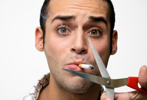 A man's cigarette about to be cut by scissors.