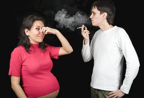 A man smokes a cigarette next to a pregnant woman.